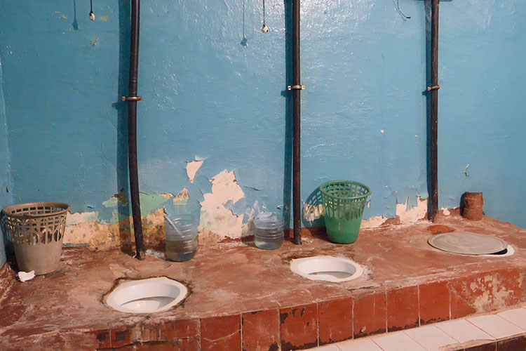 На первом этаже — деревянные полы, общий туалет в виде дырок в полу, стены, с которых обваливается штукатурка, заржавевшие раковины и только холодная вода