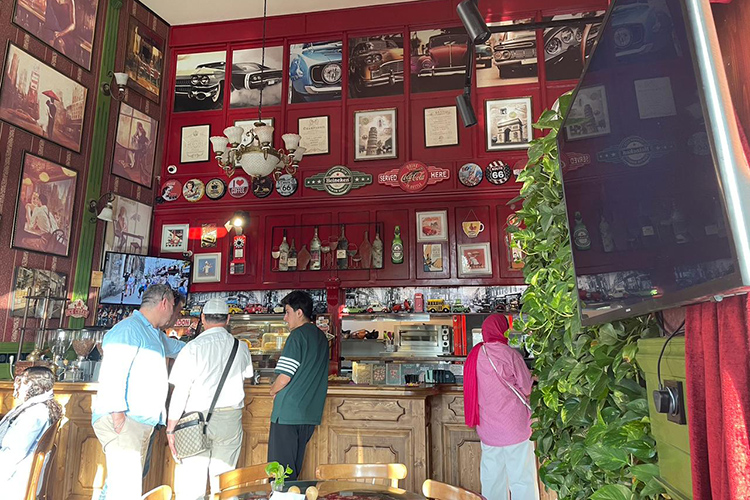 «В популярном кафе Шираза под названием Abizh Cafe по телевизору показывают мультфильм, из колонок льется спокойная западная музыка, а три молодые девушки обсуждают новый наряд за чашкой кофе и тортом»