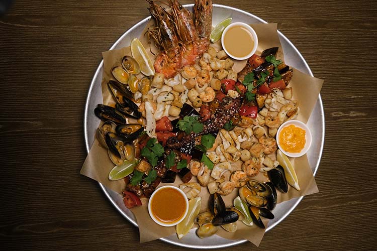 «Если хочется попробовать всю классику даров моря разом, можно заказать приготовленное на гриле „Морское ассорти“ с паназиатским салатом, этой огромной тарелки обычно хватает на четверых»