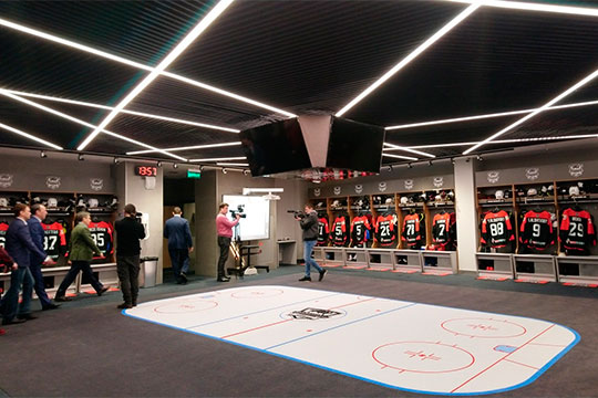 В новой раздевалке команда сидит по кругу, каждый хоккеист видит партнёра, а в центре под потолком четыре жк-панели — по одной на каждую сторону